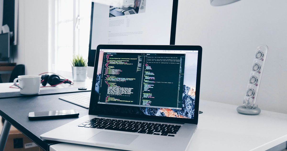 An open laptop running a code editor on a desk beside a larger monitor.